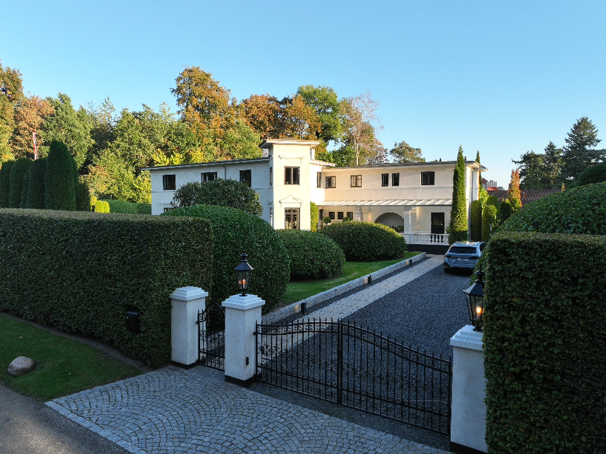 Villa Thyra seen beyond its wrought-iron gate, clipped hedges and spherical topiary framing the gravel drive in low sun