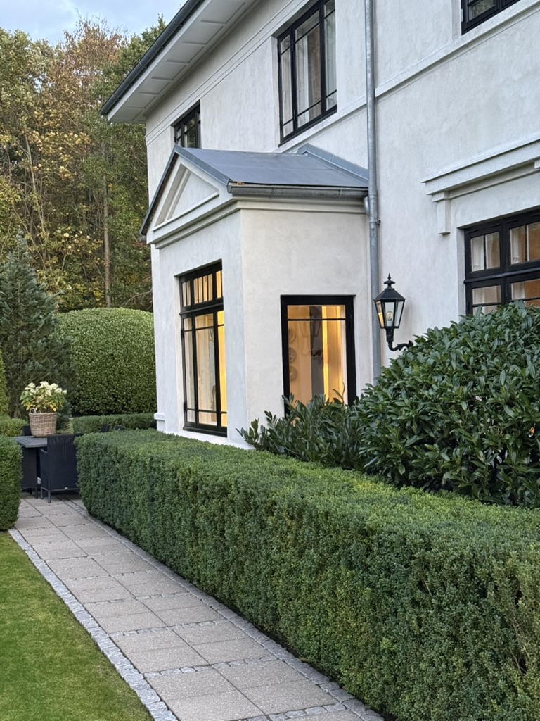 Stone garden path along sculpted hedges and the pale facade in autumn